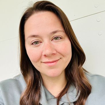 Smiling woman with long brown hair and green eyes in a gray hoodie.