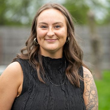 Smiling woman with tattoos in a black sleeveless top outdoors.