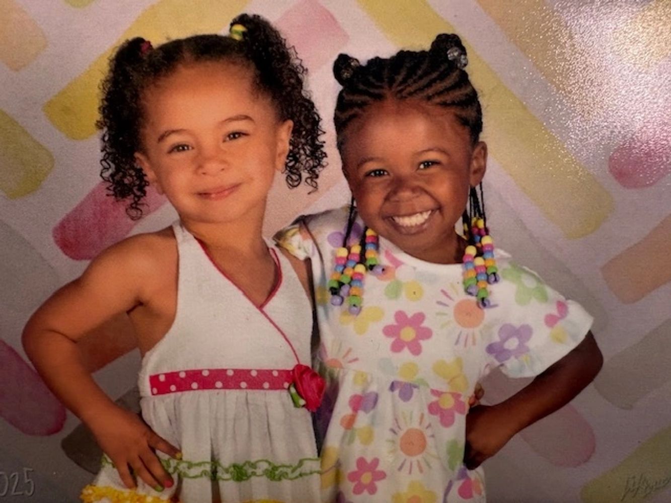 Two young girls smiling, dressed in colorful outfits with playful hairstyles.