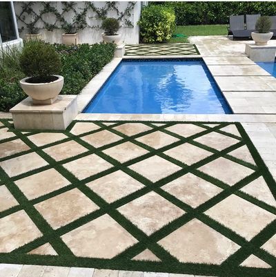 Artificial grass strips in between pavers next to a pool. 