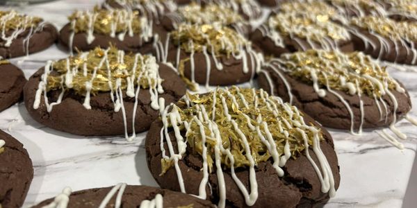 Chocolate cookies topped with white drizzle and golden sprinkles.