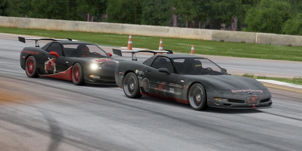 Two black sports cars racing closely on a track with orange cones in the background.