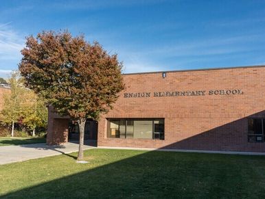 Brick building of Ensign Elementary School with tree and clear blue sky.