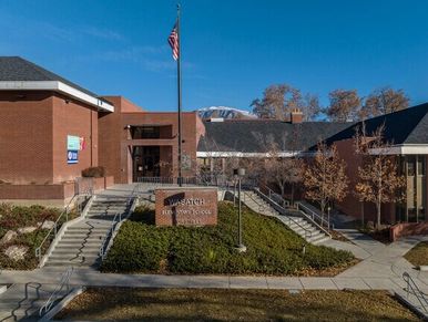 View of a college campus building with an American flag and mountain backdrop.