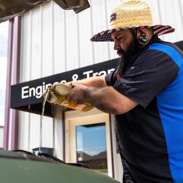 Man in a straw hat pouring liquid into a vehicle near an engineering building.