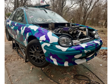 A colorful camo-painted car with its hood open, showing the engine, parked outdoors.