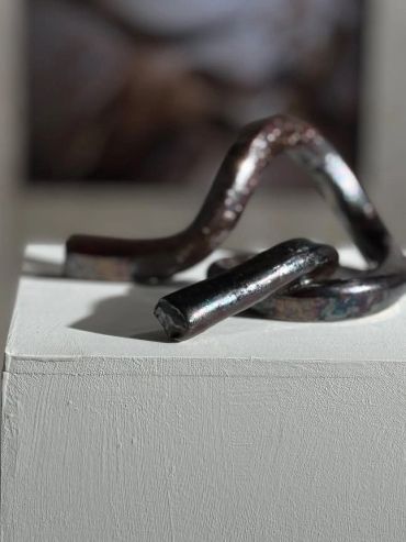 A close-up of a twisted metallic object on a white pedestal.