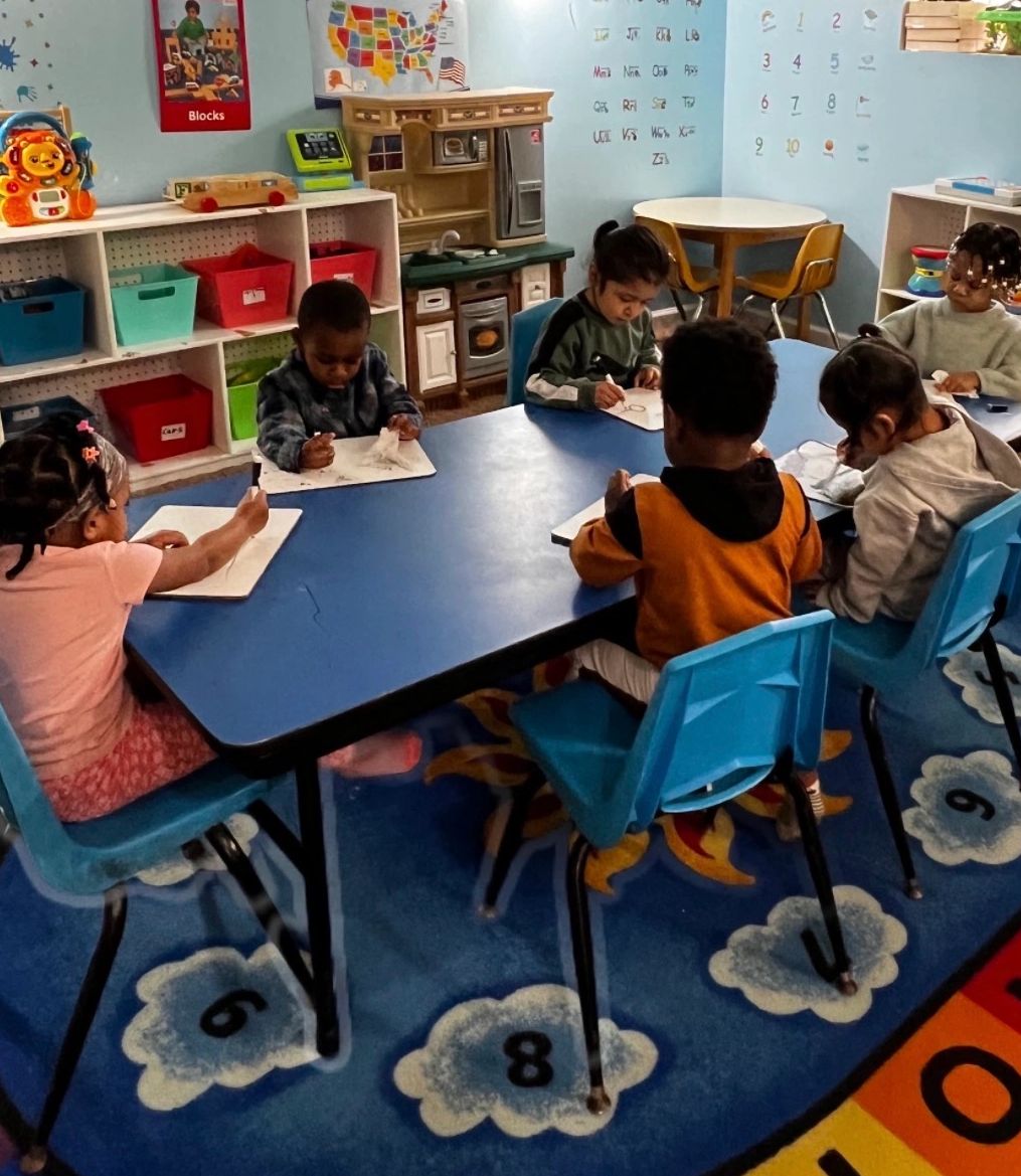 Young children sitting around a table drawing in a colorful classroom.