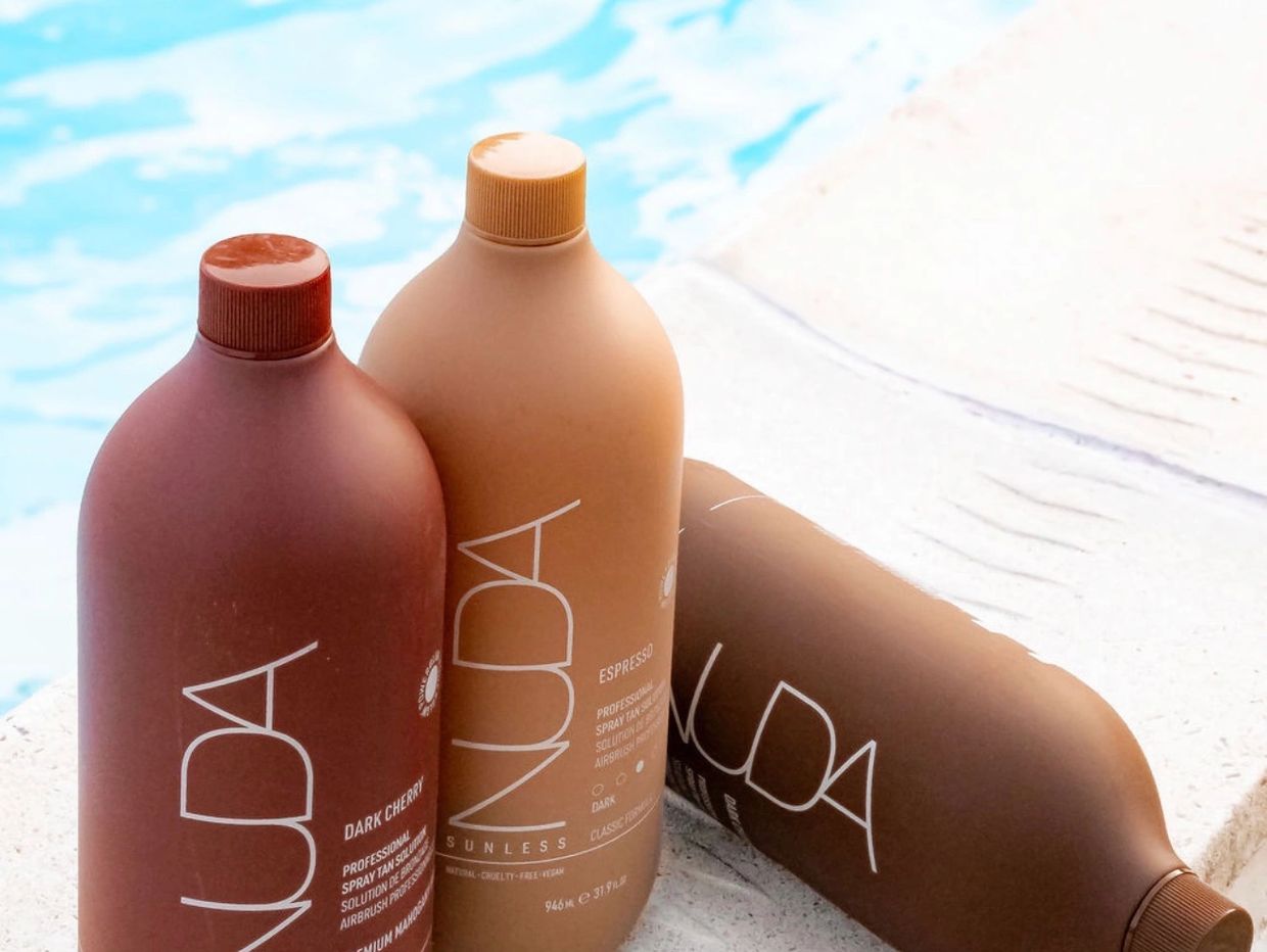 Three NUDA sunless spray tan bottles near a pool.