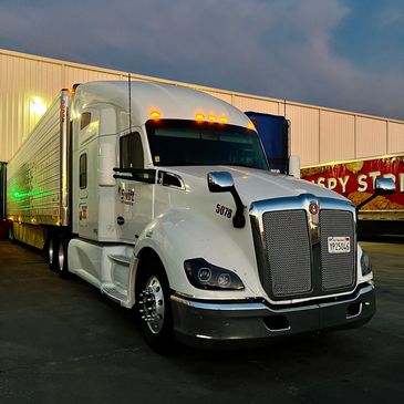 White semi-truck parked outside a warehouse at dusk.