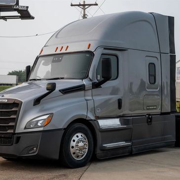 A silver Freightliner semi-truck parked on a concrete surface with a trailer.