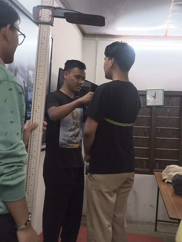 Two men measuring height and chest circumference indoors.