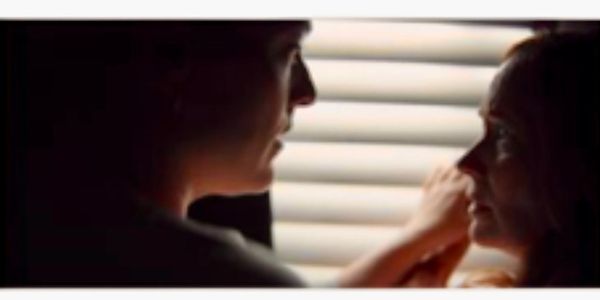 Two people looking at each other softly near a window with blinds.