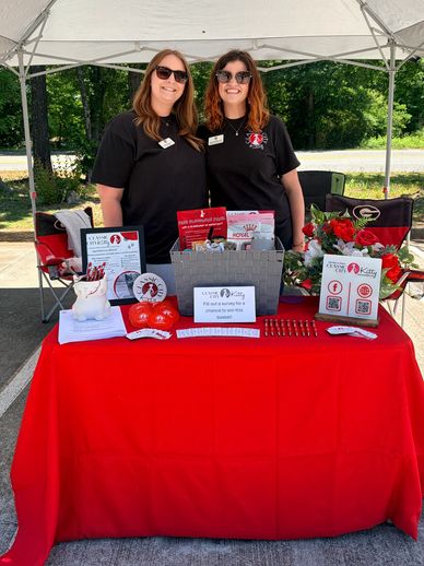 Two women at an informational booth with red tablecloth and promotional items.