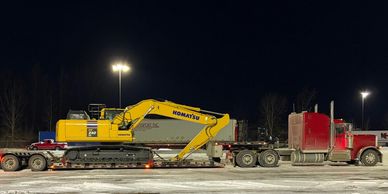 A red truck transporting a yellow Komatsu excavator at night.