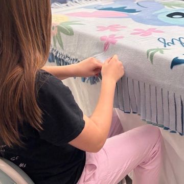 Person tying knots on the fringe of a colorful fleece blanket.