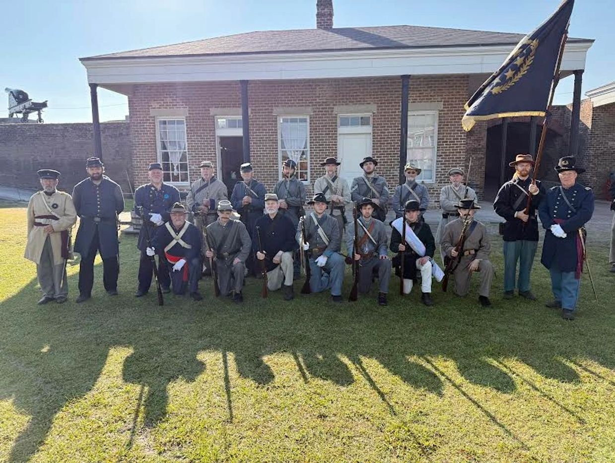 Group of men in historic military uniforms posing outside a brick building.