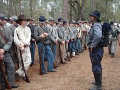 A group of Civil War reenactors in uniform standing in formation outdoors.
