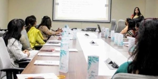 Woman leading a meeting with attendees seated around a conference table.
