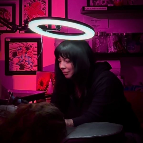 A woman with a glowing ring light above her head in a dim pink-lit room.