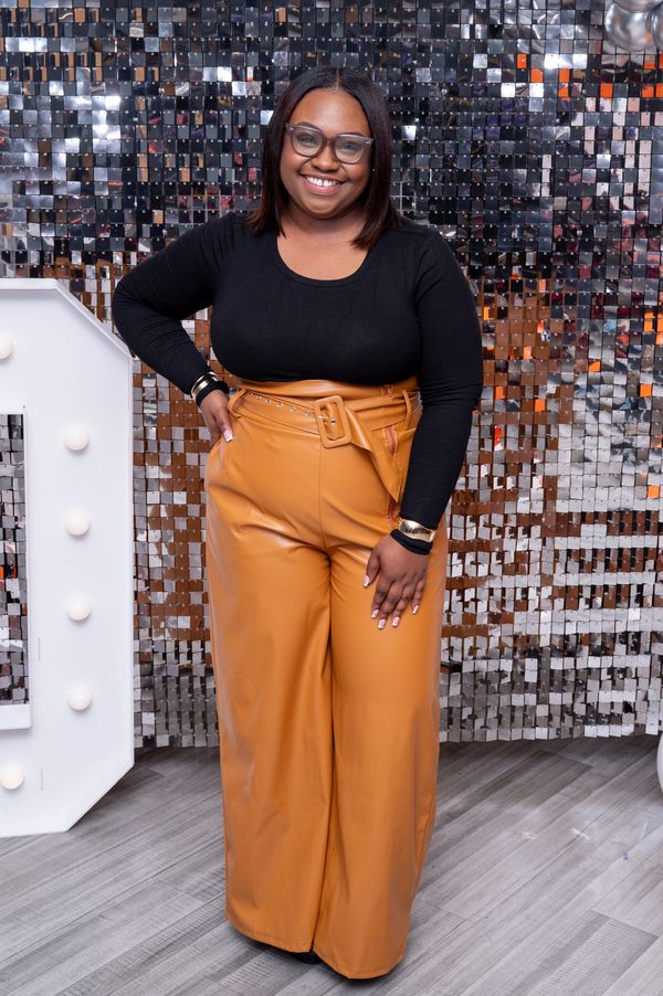 Woman smiling in black top and tan wide-leg pants.