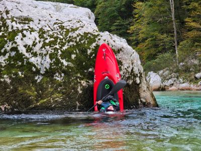 Person kayaking upside down near a rocky shore.