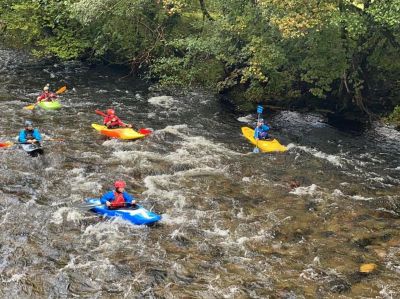 Group kayaking on a river with rocky shores.