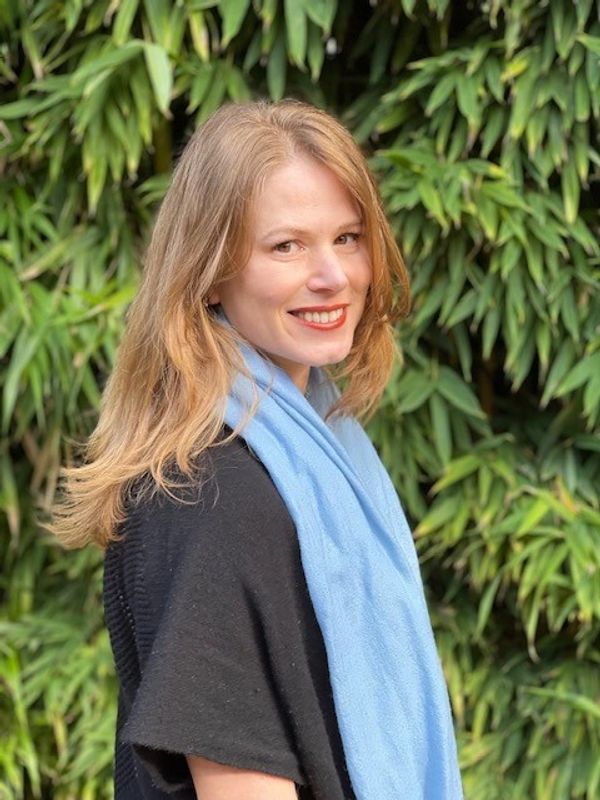 Smiling woman with blonde hair and a blue scarf poses outdoors.