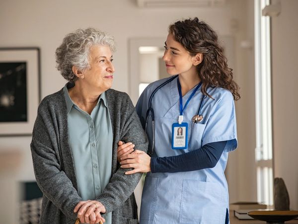 Young caregiver helping senior woman walking. Nurse assisting her old woman patient at nursing home.