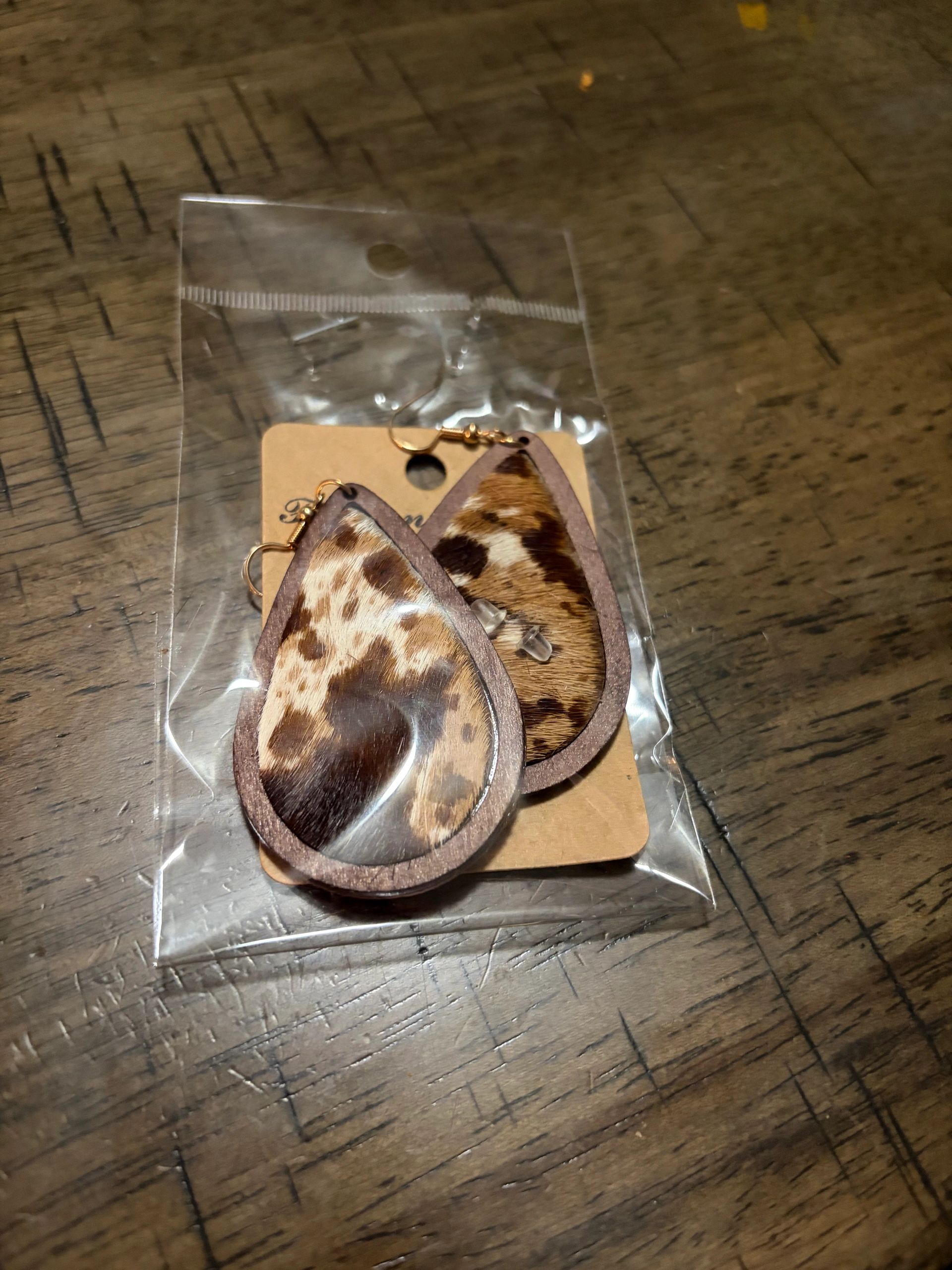 Teardrop-shaped animal print earrings in plastic packaging on a wooden table.