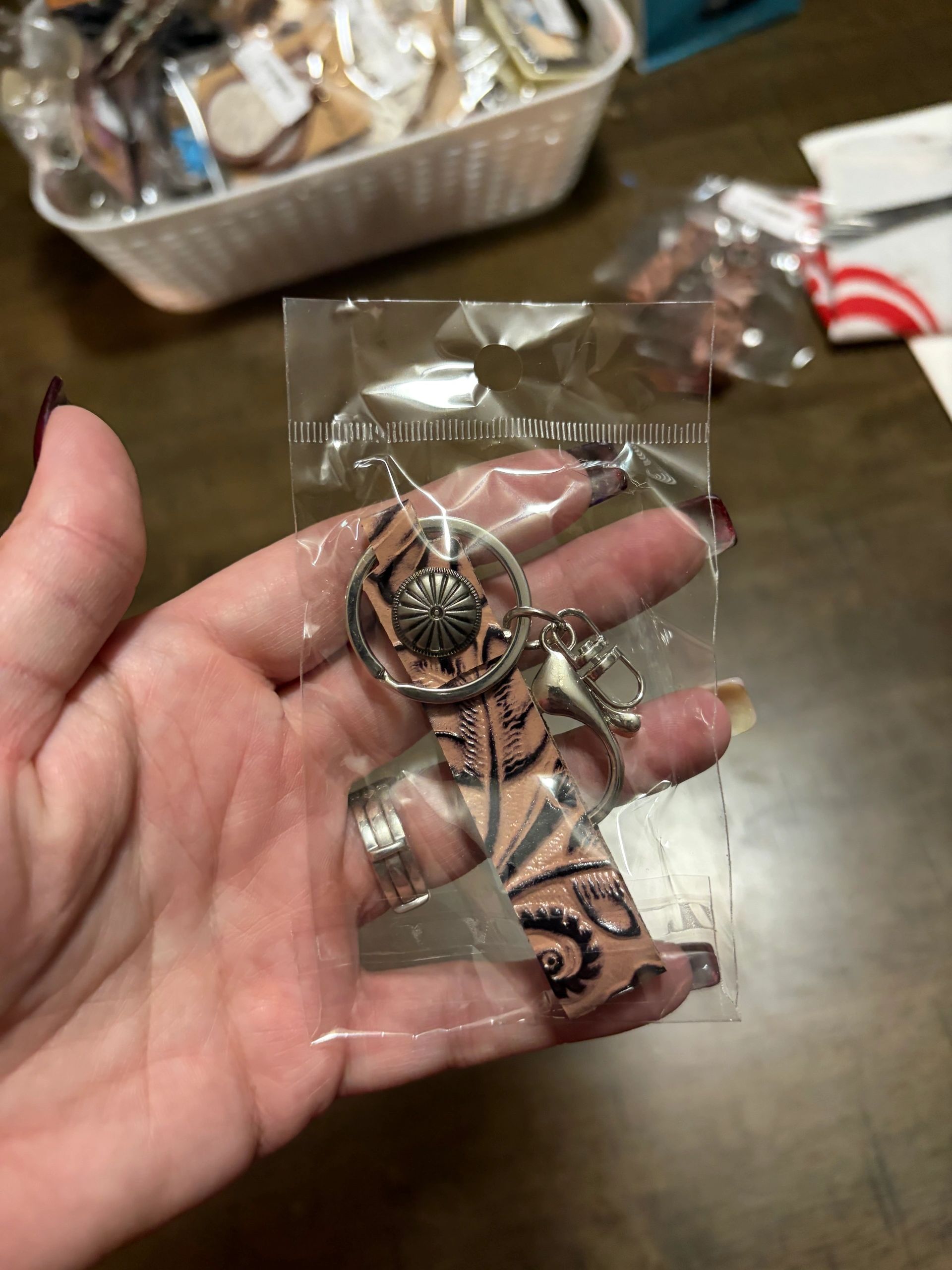 Hand holding a packaged leather keychain with metal details.
