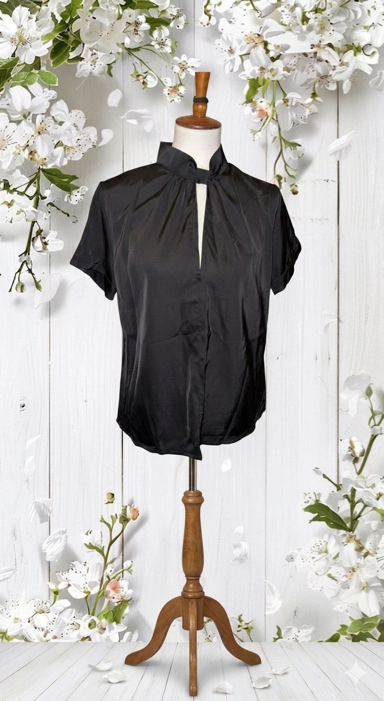Elegant black satin blouse on a wooden mannequin with floral background.
