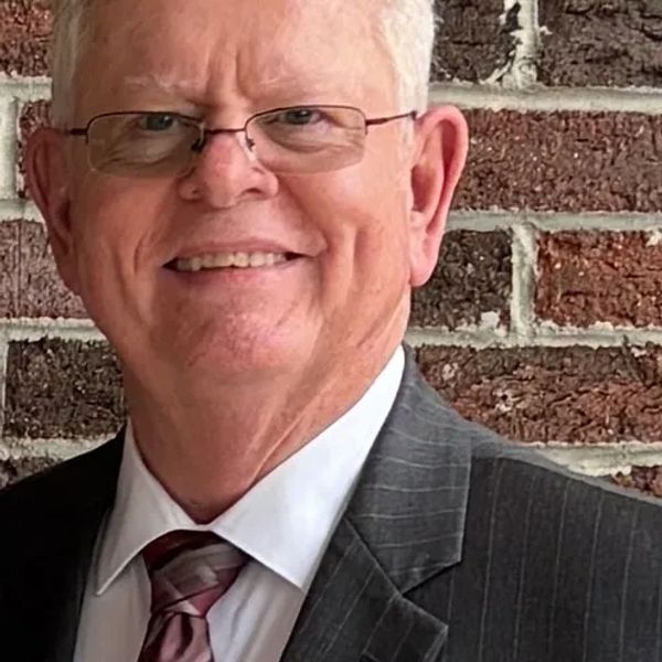 Smiling elderly man in suit and tie against brick wall.