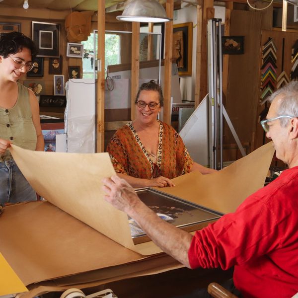 Alex, Lesli, and Vanessa Uribe wrapping finished framed painting in silver and blue frame