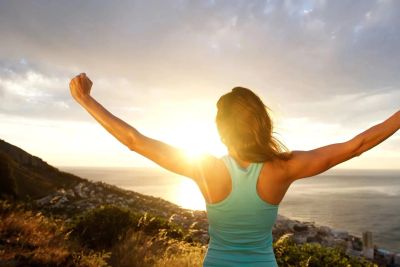 Woman celebrating with arms outstretched at sunrise.