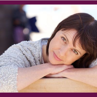 Woman in her 40's, arms crossed, lying her head on her hands, looking content with life.