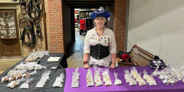 A woman wearing a blue pirate hat, white blouse and black corset, standing behind a table of sweets