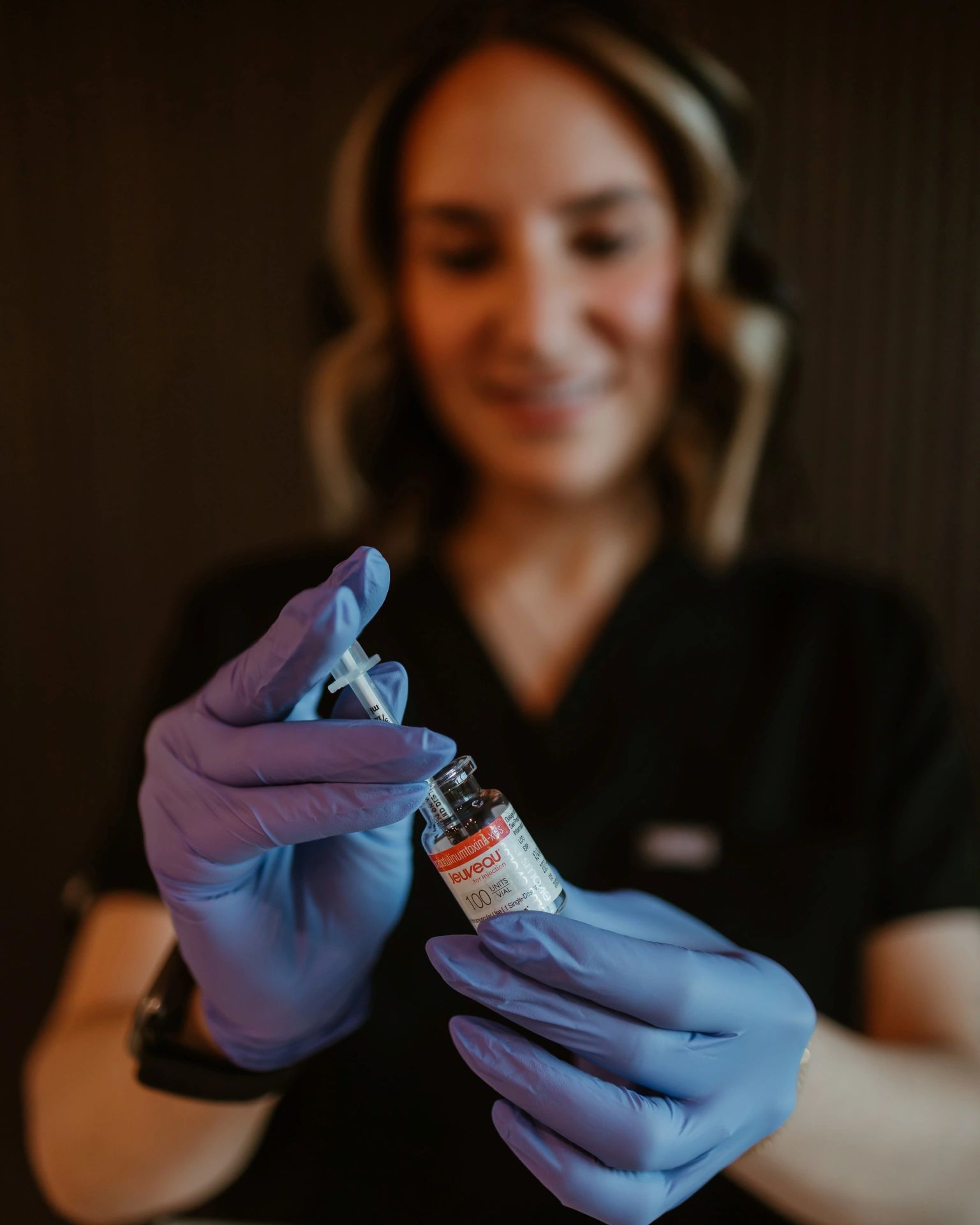 A person in blue gloves prepares a syringe with a vial labeled Jeuveau.
