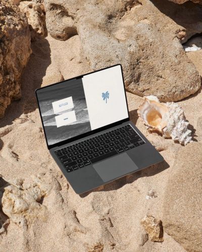 Laptop lying on sandy beach near seashells.