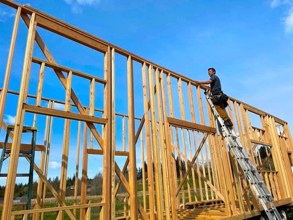 Framing a handcrafted, custom tiny home for simple living in the PNW.  Worker uses a ladder.