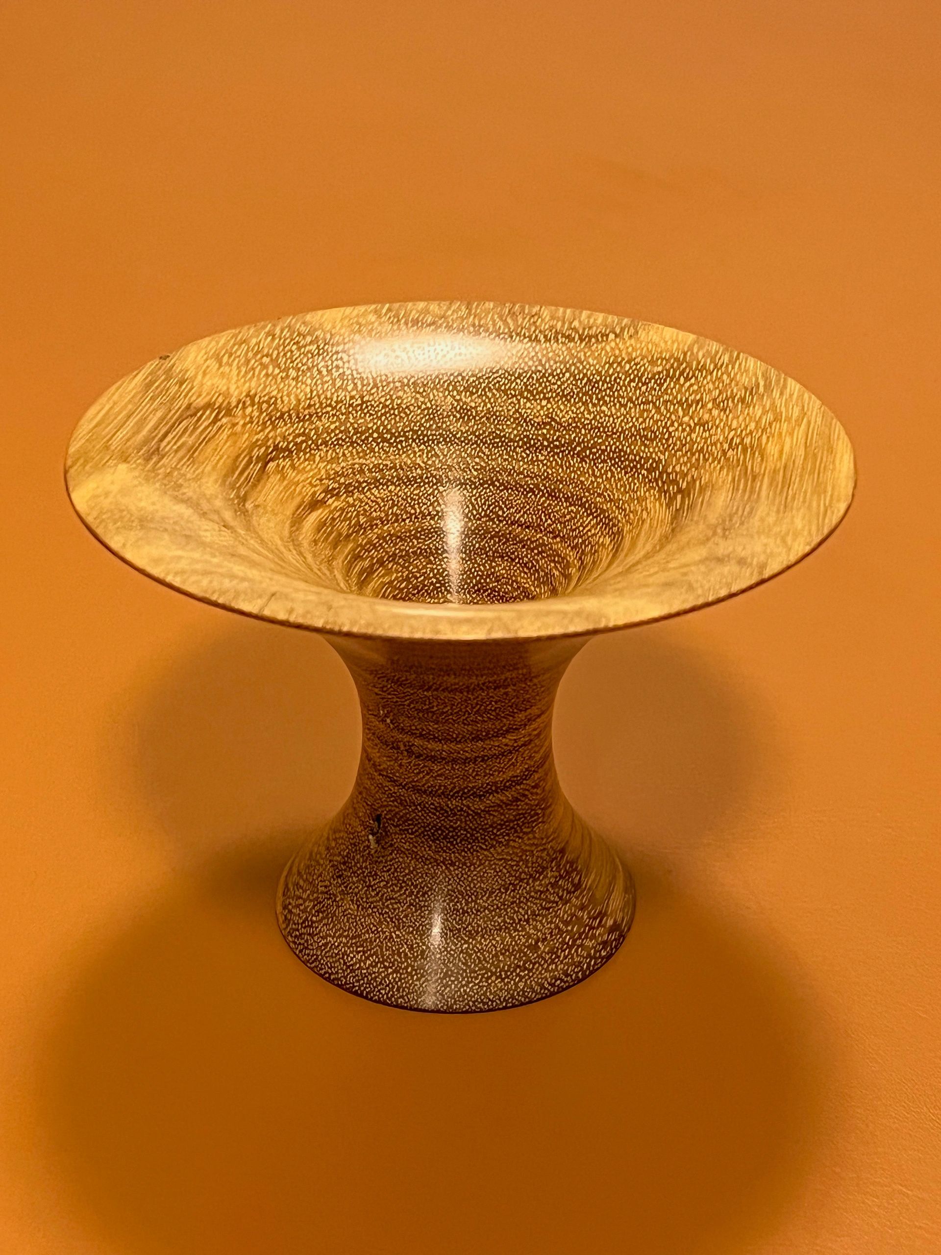A polished wooden vase with intricate grain patterns against an orange backdrop.