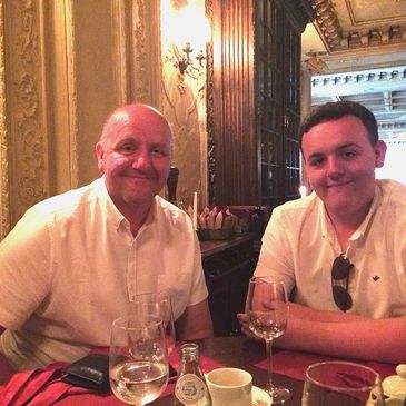 Two men smiling at a restaurant table with drinks and a warm ambiance.