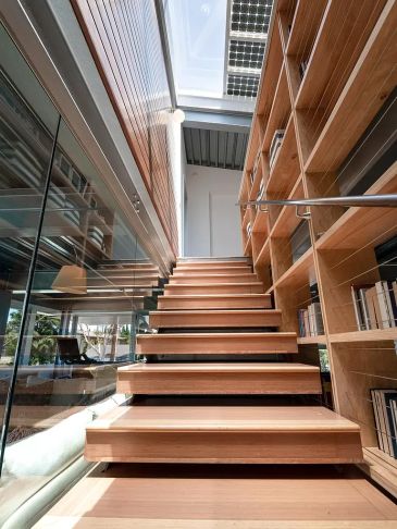 Modern wooden staircase with built-in bookshelves and glass wall.