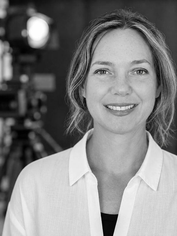 Smiling woman in white shirt in front of blurred camera.