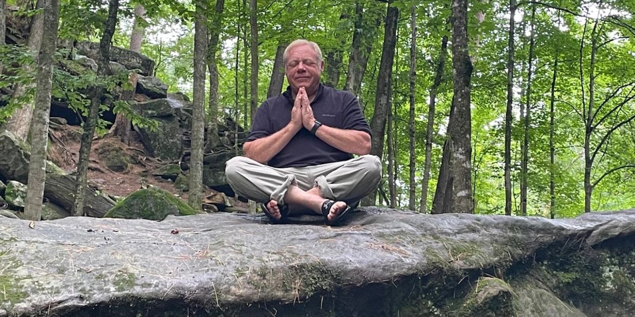 Man meditating in forest on a large rock.