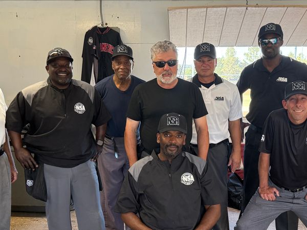 Group of nine men in NSA sports uniforms posing indoors.