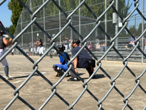 View through a chain-link fence of a youth baseball game in action.