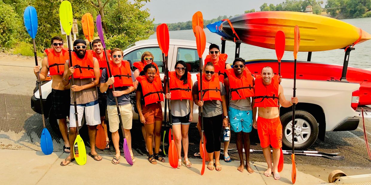 Group of friends in life jackets holding paddles ready for kayaking by the lake.