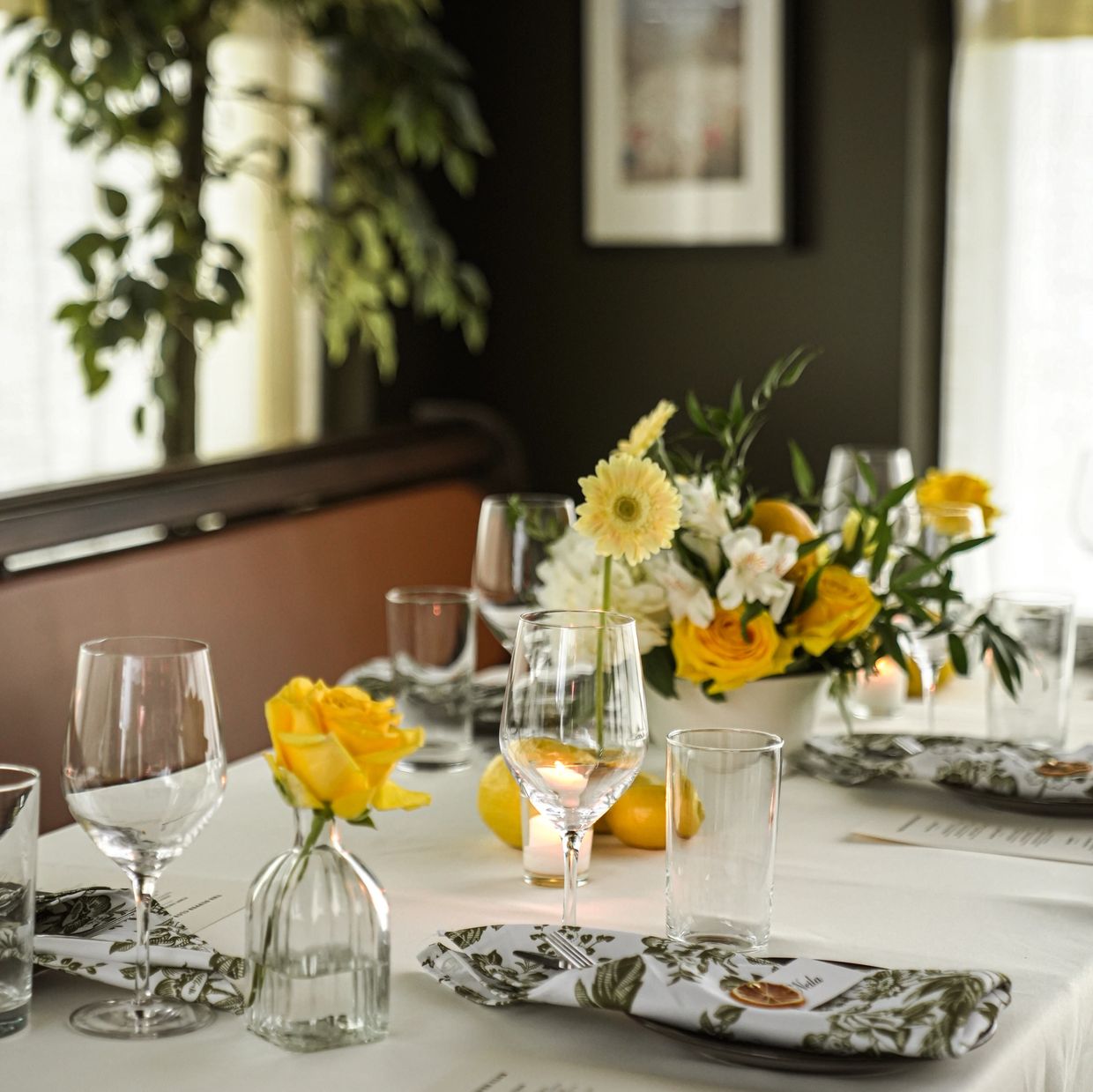 Elegant table setting with yellow roses and floral napkins on a white tablecloth.