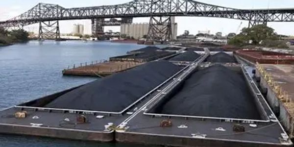 Coal barges docked under a large steel bridge over a river.